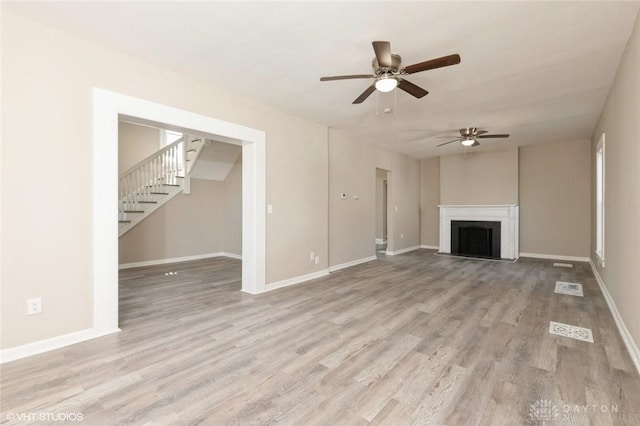 unfurnished living room with wood finished floors, ceiling fan, baseboards, and stairs