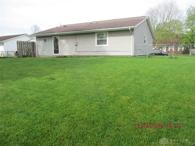 rear view of property featuring fence and a lawn