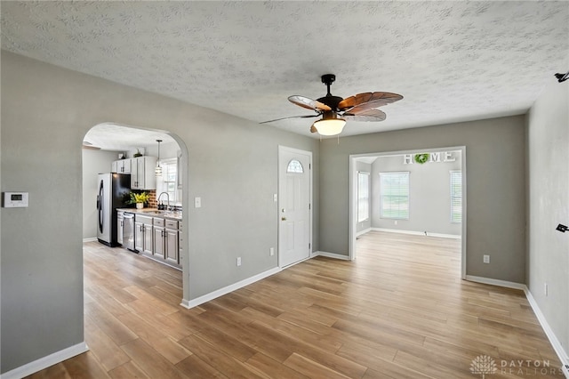 foyer entrance featuring ceiling fan, light wood-style flooring, a textured ceiling, baseboards, and arched walkways