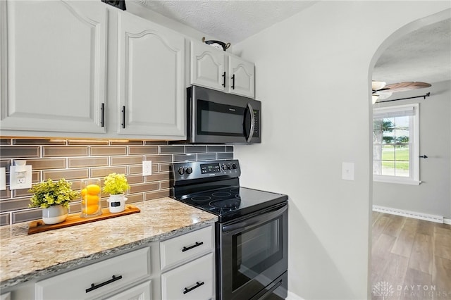 kitchen featuring tasteful backsplash, arched walkways, stainless steel microwave, white cabinetry, and black electric range oven