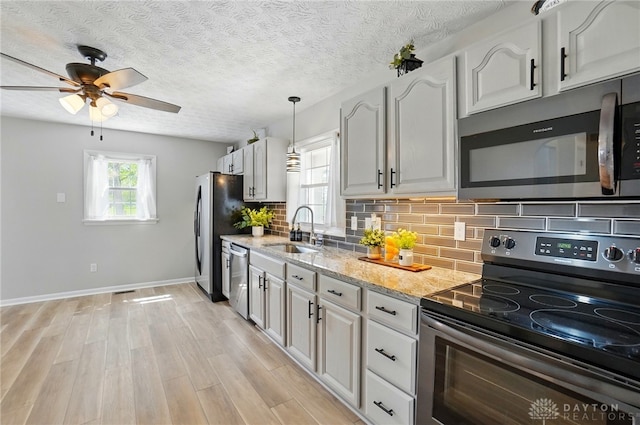 kitchen with light wood-style flooring, decorative backsplash, stainless steel appliances, a sink, and a ceiling fan