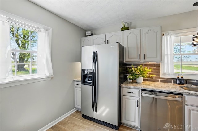 kitchen featuring light stone countertops, backsplash, stainless steel appliances, and a healthy amount of sunlight