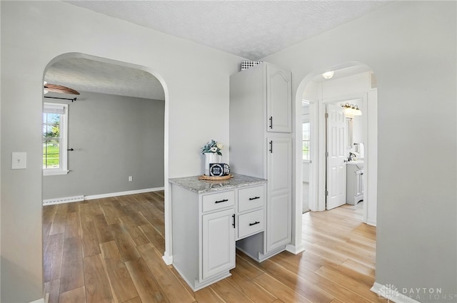 hallway with baseboards, arched walkways, light wood-style floors, and a textured ceiling