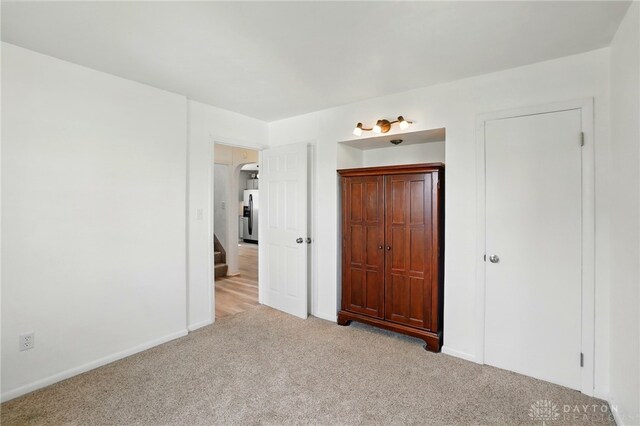 unfurnished bedroom featuring stainless steel refrigerator with ice dispenser, light carpet, and baseboards