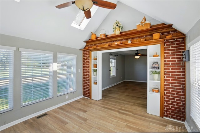 spare room with a skylight, ceiling fan, baseboards, light wood-type flooring, and high vaulted ceiling