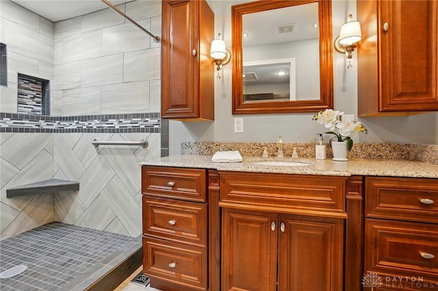 bathroom featuring a tile shower, vanity, and visible vents
