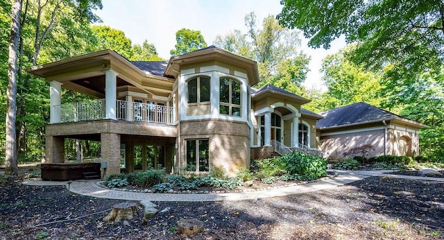 back of house with brick siding, a balcony, and a hot tub