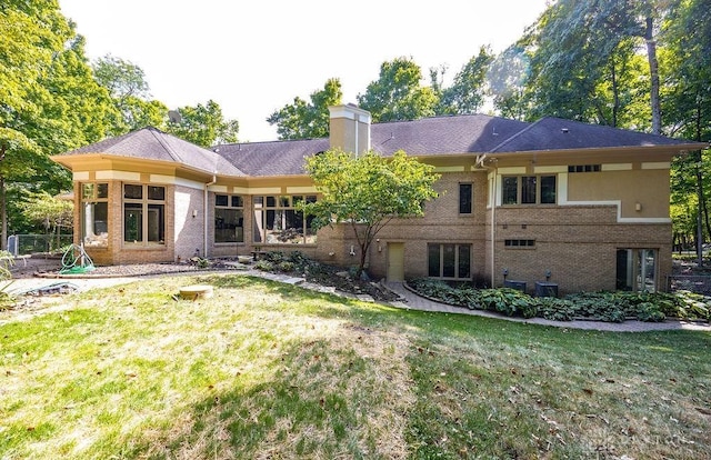 back of house with a chimney, brick siding, and a yard