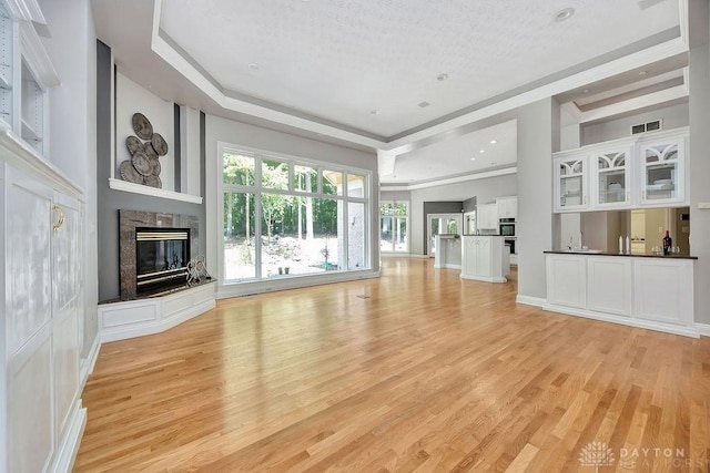 unfurnished living room with visible vents, light wood-style flooring, a raised ceiling, and a glass covered fireplace