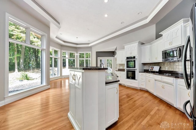 kitchen with a kitchen island with sink, stainless steel appliances, backsplash, white cabinetry, and a tray ceiling