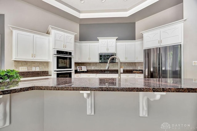 kitchen featuring white cabinetry, a kitchen breakfast bar, backsplash, and appliances with stainless steel finishes