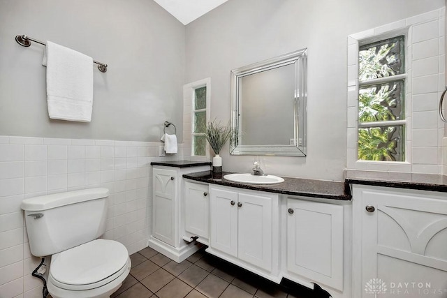 bathroom with tile walls, vanity, toilet, tile patterned flooring, and wainscoting