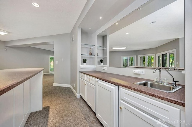 kitchen featuring white cabinets, light carpet, dark countertops, a sink, and visible vents