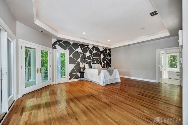 unfurnished living room with an accent wall, a raised ceiling, wood-type flooring, baseboards, and french doors
