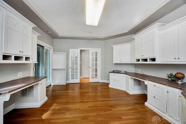 unfurnished office with wood finished floors, built in study area, baseboards, visible vents, and french doors