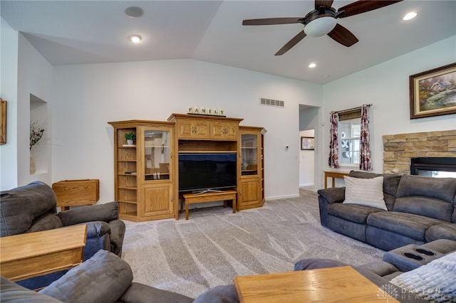 living area with a ceiling fan, a stone fireplace, visible vents, vaulted ceiling, and light carpet