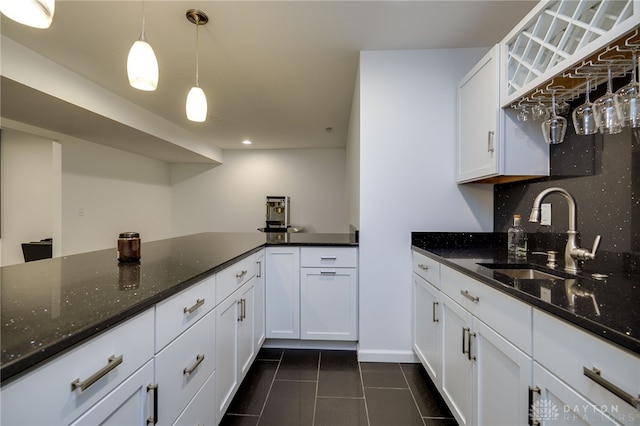 kitchen featuring hanging light fixtures, a sink, dark stone counters, white cabinetry, and dark tile patterned floors