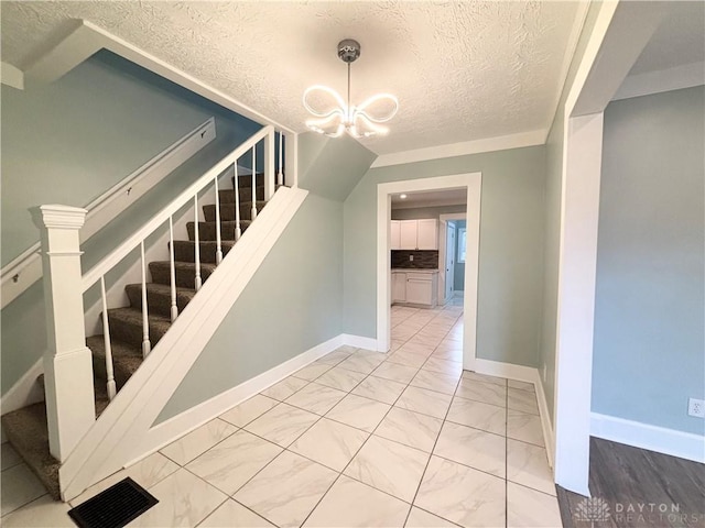 stairs with a textured ceiling, a notable chandelier, marble finish floor, and baseboards