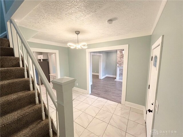 stairs featuring marble finish floor, a notable chandelier, a textured ceiling, and baseboards