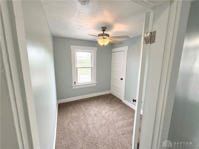 carpeted empty room with baseboards, ceiling fan, and a textured ceiling