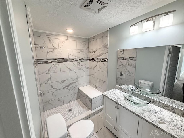 bathroom featuring tiled shower, vanity, toilet, visible vents, and a textured ceiling