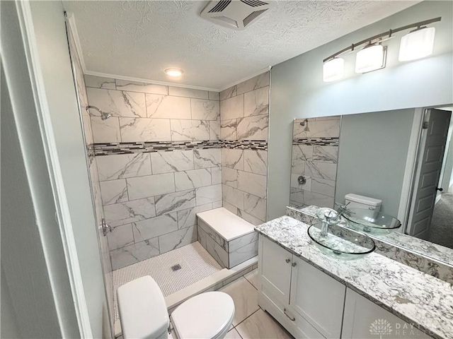 bathroom featuring a tile shower, toilet, vanity, visible vents, and a textured ceiling