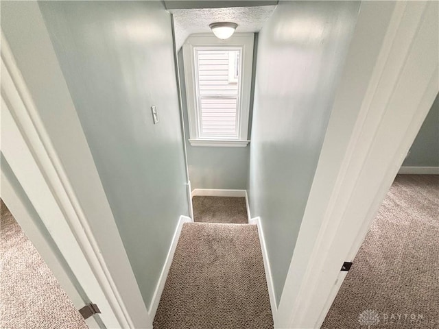 stairway with a textured ceiling, carpet flooring, and baseboards