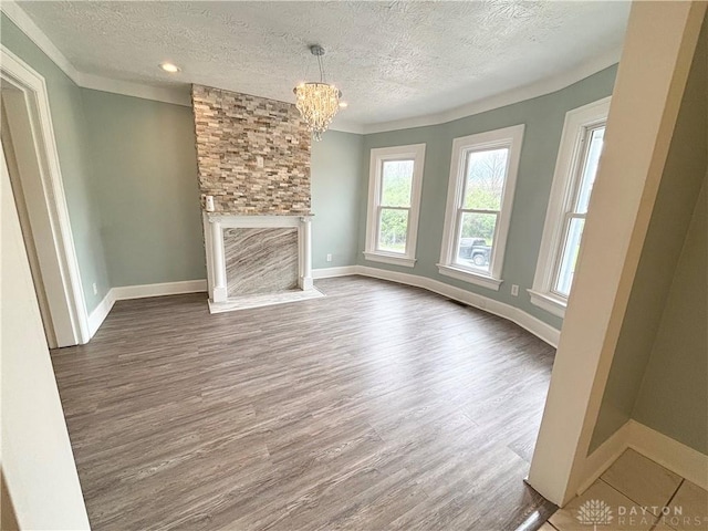 unfurnished living room with wood finished floors, a chandelier, baseboards, a textured ceiling, and a fireplace with flush hearth