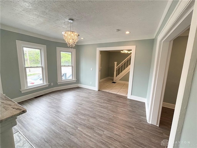 unfurnished dining area featuring stairway, a notable chandelier, baseboards, a textured ceiling, and wood finished floors