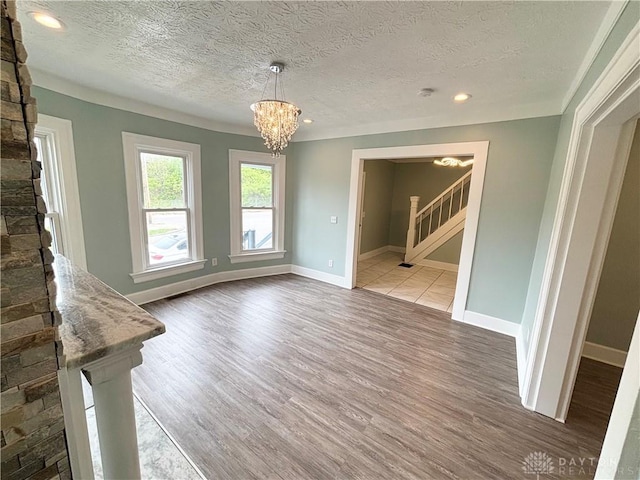 unfurnished dining area with a textured ceiling, an inviting chandelier, stairway, and wood finished floors