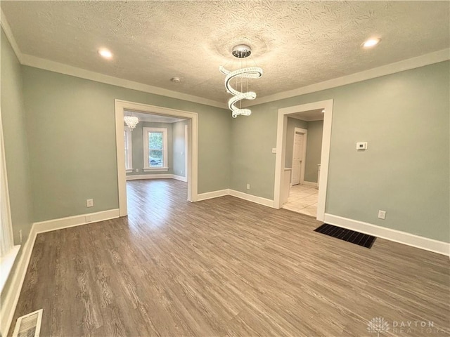empty room featuring a textured ceiling, visible vents, wood finished floors, and a notable chandelier