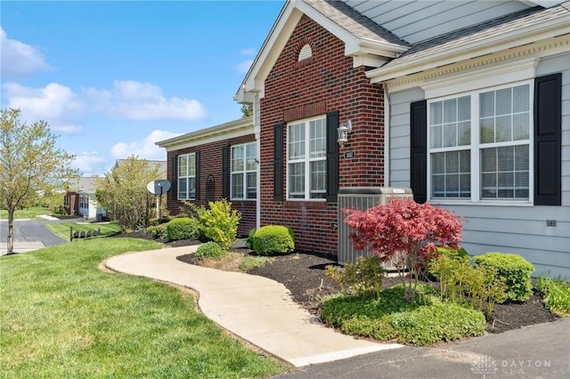 view of side of home with a lawn, central AC, a shingled roof, and brick siding