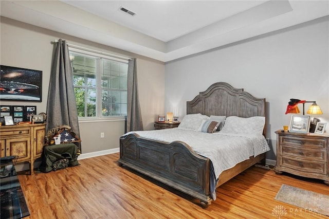 bedroom featuring baseboards, visible vents, wood finished floors, and a raised ceiling