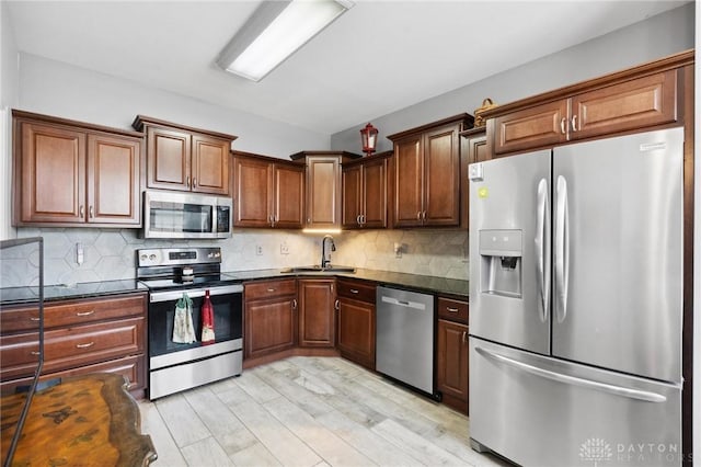 kitchen with stainless steel appliances, backsplash, light wood-style flooring, and a sink