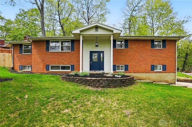 raised ranch featuring brick siding, fence, and a front lawn