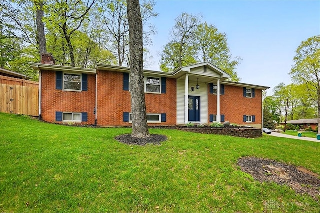 split foyer home with fence, a chimney, brick siding, and a front lawn