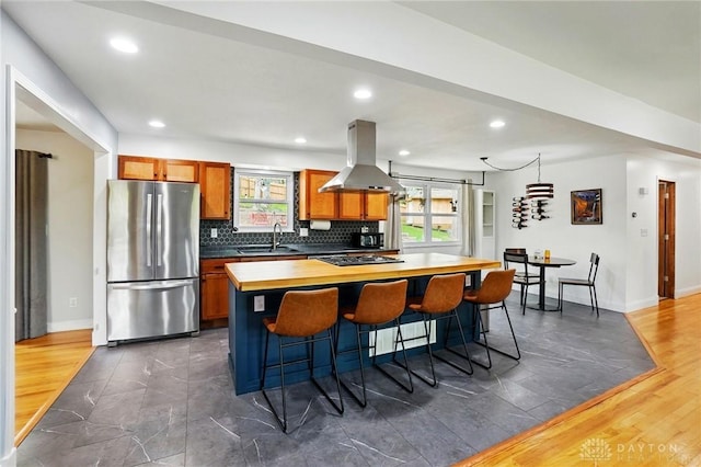 kitchen featuring island range hood, freestanding refrigerator, brown cabinetry, a sink, and a kitchen breakfast bar