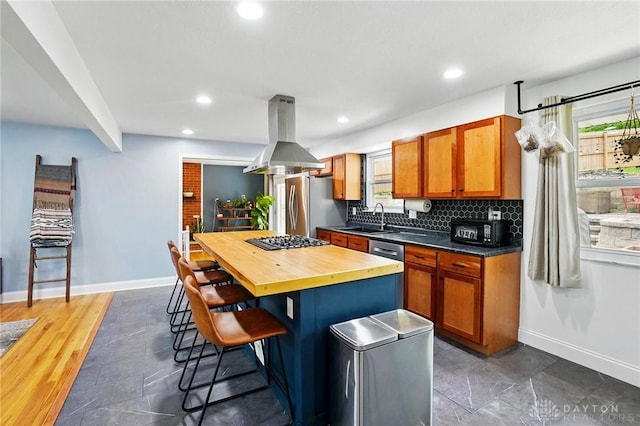 kitchen with a sink, wood counters, island exhaust hood, a breakfast bar, and baseboards