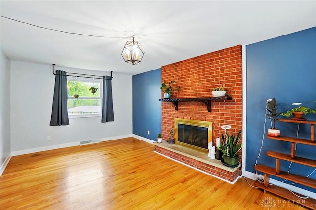 unfurnished living room featuring a chandelier, a fireplace, visible vents, baseboards, and wood finished floors
