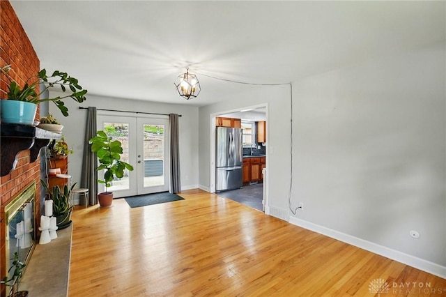 foyer with french doors, baseboards, a fireplace, wood finished floors, and a notable chandelier