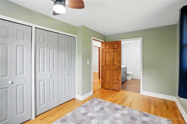 unfurnished bedroom featuring ceiling fan, baseboards, light wood-type flooring, multiple closets, and ensuite bath