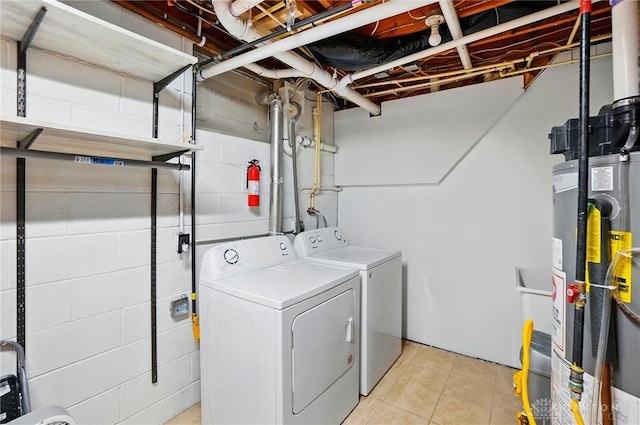 clothes washing area featuring concrete block wall, water heater, washing machine and clothes dryer, and laundry area
