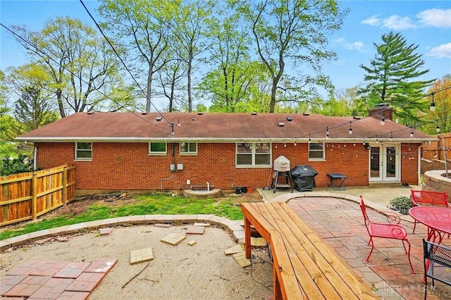 back of property with a patio, brick siding, a chimney, french doors, and fence