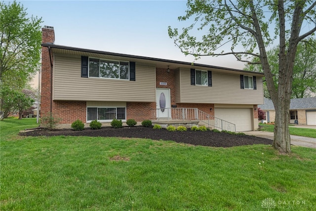 split foyer home featuring a chimney, brick siding, a front yard, concrete driveway, and an attached garage