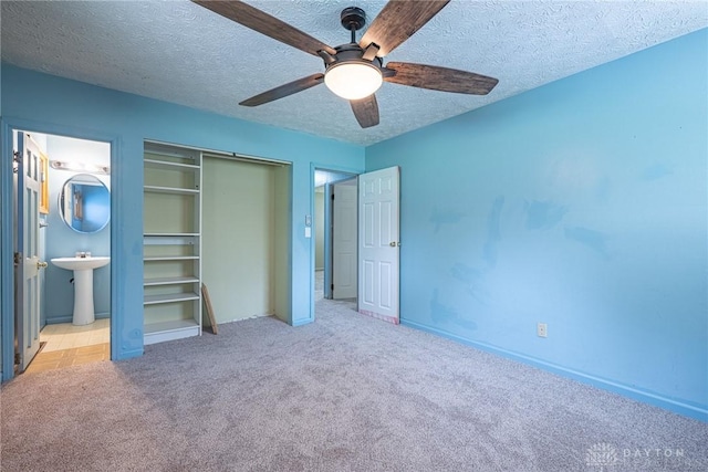 unfurnished bedroom featuring a closet, carpet, ceiling fan, a sink, and a textured ceiling