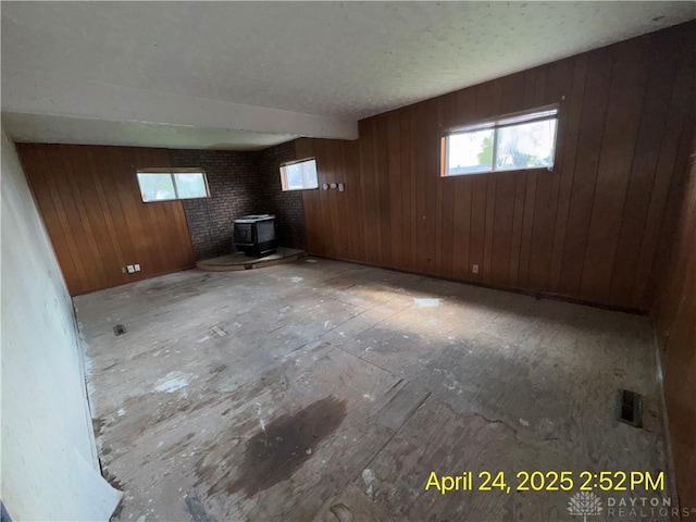 basement featuring wood walls, visible vents, and a wood stove