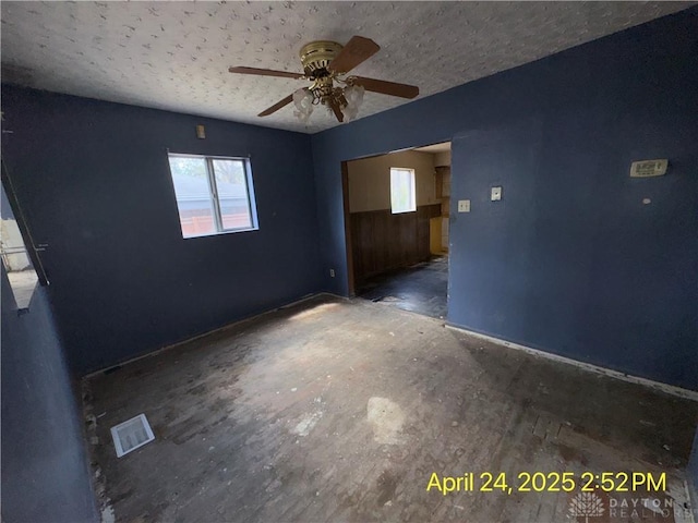 empty room with a textured ceiling, visible vents, a ceiling fan, and baseboards