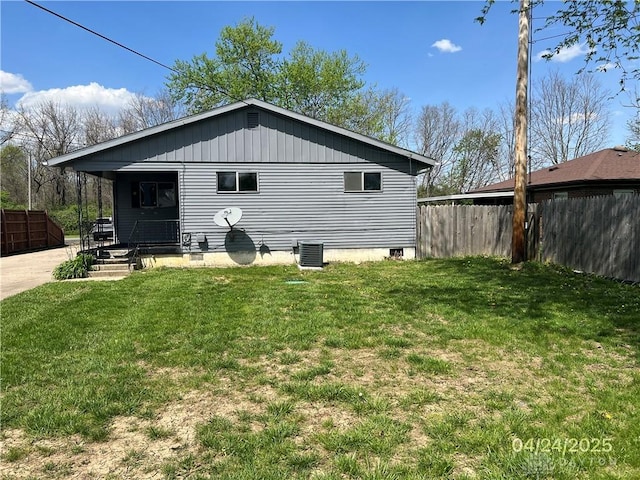 rear view of property with a lawn, central AC unit, and fence
