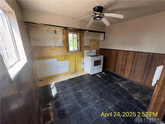 kitchen with white electric range oven, wooden walls, ceiling fan, and wainscoting
