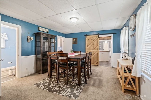 dining room featuring carpet flooring, a barn door, wainscoting, and a paneled ceiling